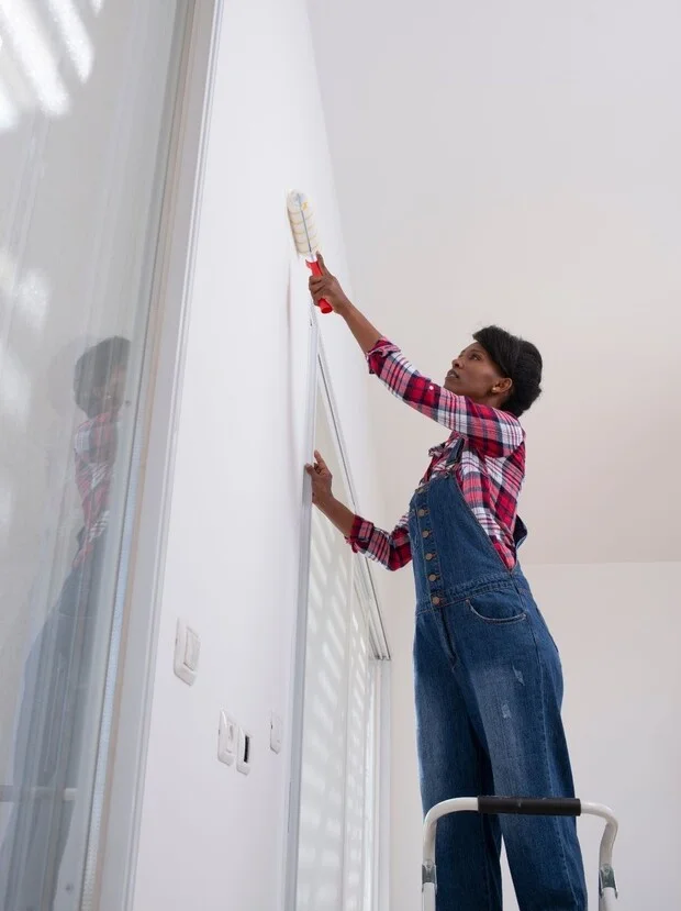 Woman painting interior wall using a roller while standing on a ladder, showcasing professional painting skills relevant to residential services in Hopewell Township.