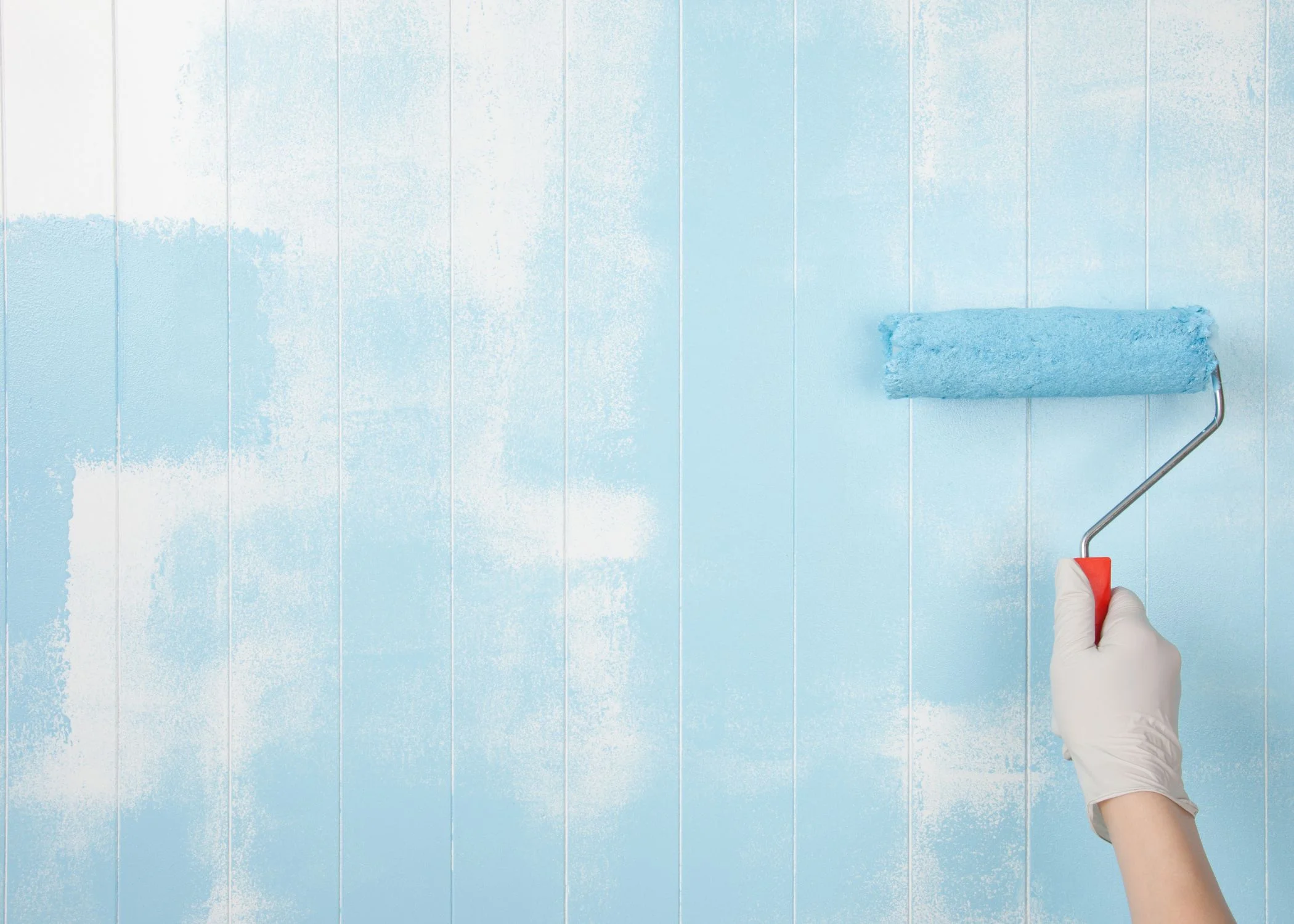 Hand holding a paint roller applying light blue paint on a wooden panel wall, illustrating professional painting services in Hopewell Township.